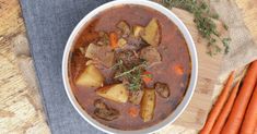 a bowl filled with stew and carrots on top of a wooden table next to a spoon