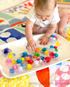 a baby is playing with colorful candies on a tray