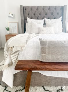 a bed with white linens and pillows in a small room next to a wooden bench