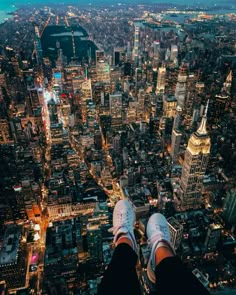 someone standing on top of a tall building with their feet up in the air over a city at night