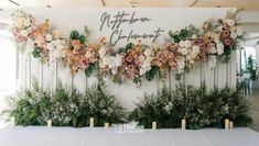 an arrangement of flowers and greenery is displayed on the wall behind a table with candles