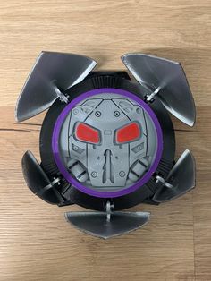 an overhead view of a robot from above on a wooden floor with metal blades and red eyes