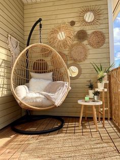 a hanging egg chair on a porch with pillows and throw pillows in the sun, next to a side table