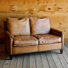 a brown leather couch sitting on top of a wooden floor next to a wood wall