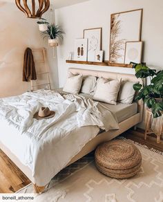 a bed with white sheets and pillows in a bedroom next to a potted plant