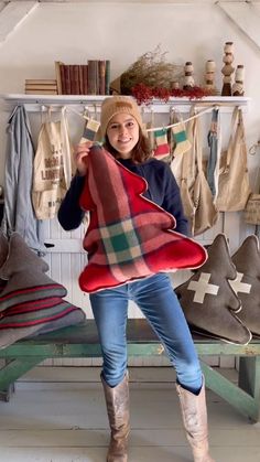 a woman standing in front of a bench holding up a plaid blanket