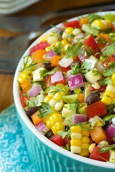 a bowl filled with corn and vegetables on top of a blue table cloth next to a fork