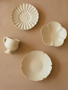 three white dishes sitting next to each other on a brown tableclothed surface with one bowl and two plates