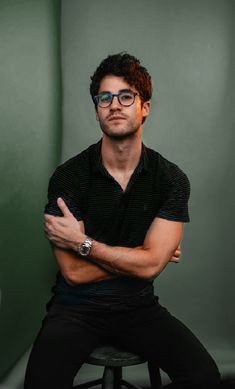 a man sitting on top of a stool with his arms crossed in front of him