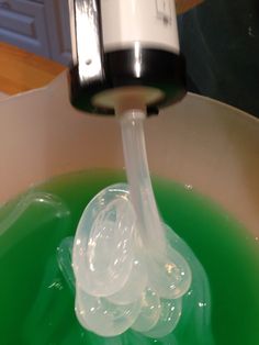 a green liquid is being poured into a white bowl with a black and silver faucet