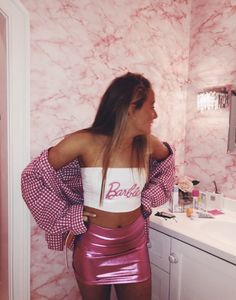 a woman standing in front of a bathroom mirror wearing a pink skirt and crop top