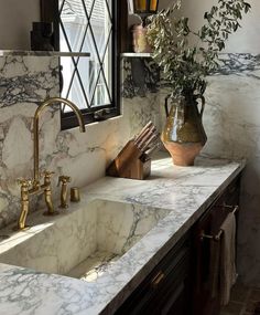 a bathroom with marble counter tops and gold faucets on the sink, along with a vase filled with greenery