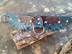 a leather belt with feathers on it sitting on top of a piece of tree bark