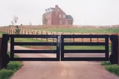 an open gate leading to a large house on a farm with a horse in the background