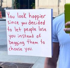 a person holding a cell phone in front of a sign that says you look happy since you decided to let people lose you instead of begging them to choose you