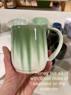 a hand holding a green and white coffee mug with the words honey fix x3 with small blobs of seaweed on the outer rim