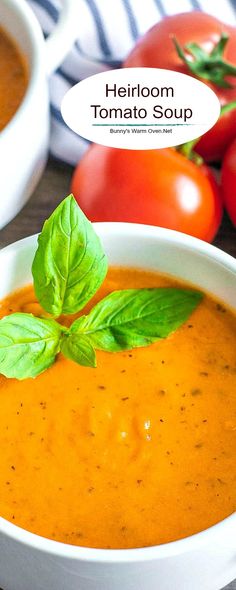 there is a bowl of tomato soup with basil on the top and tomatoes in the background