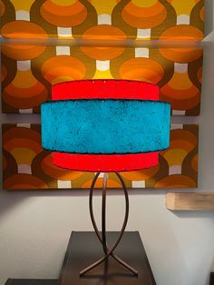 a blue and red lamp sitting on top of a metal stand in front of a painting