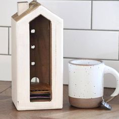 a coffee mug sitting next to a wooden birdhouse shaped like a house with holes in it