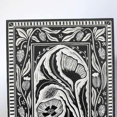 a black and white drawing of flowers in a square frame on a table with a vase next to it