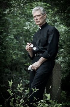 an older man is sitting on a rock and holding something in his hand while looking at the camera