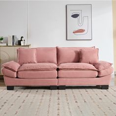 a pink couch sitting on top of a wooden floor next to a painting and rug