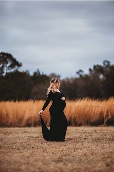 a pregnant woman in a black dress sitting on the ground with her hands behind her back