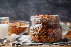 a glass jar filled with granola sitting on top of a table next to two glasses