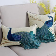 two pillows with peacocks on them sitting on a couch next to a vase filled with flowers