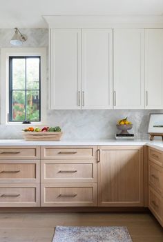 a bowl of fruit is on the counter in this white and light wood - paneled kitchen