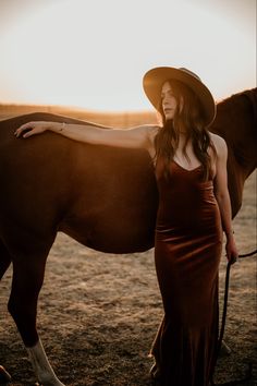 a woman standing next to a brown horse wearing a cowboy hat and holding the bridle