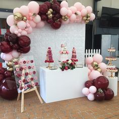 a table topped with lots of pink and red balloons next to a wall covered in cake