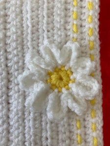 a crocheted white and yellow blanket with a flower on the front, sitting on a red surface