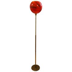 a floor lamp with a red marble ball on it's base and a gold metal pole