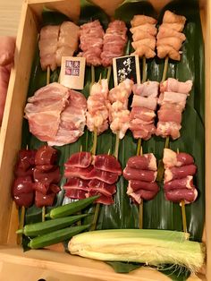 an assortment of meats and vegetables are displayed in a wooden box with chopsticks