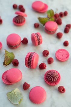 pink macaroons and raspberries on a white marble surface with green leaves