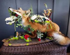 a stuffed fox is sitting on top of a wicker basket with flowers and leaves