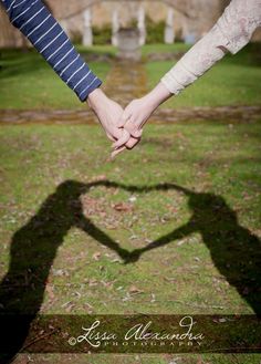 two people holding hands in the shape of a heart on top of grass and trees