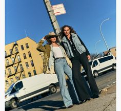 two women standing next to each other on the side of a road near a street sign