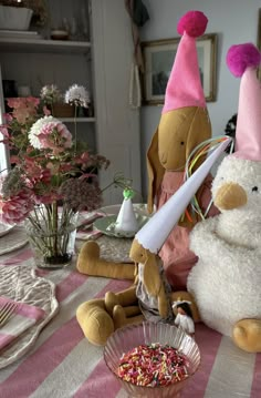 two stuffed animals sitting on top of a pink and white striped table cloth next to a bowl of sprinkles