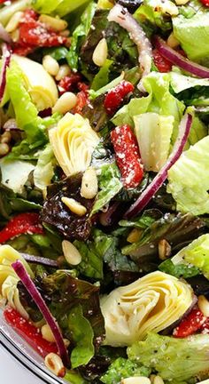 a salad with lettuce, red onions and pine nuts in a glass bowl