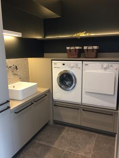 a washer and dryer in a small room with tile flooring, white cabinets and gray walls