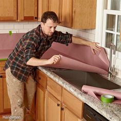 a man standing in front of a kitchen sink next to a pink sheet of paper