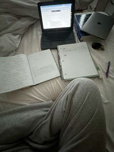 an open laptop computer sitting on top of a bed next to notebooks and books