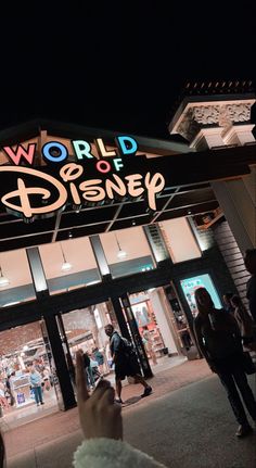 people are walking in front of the world of disney store at night with their hands up