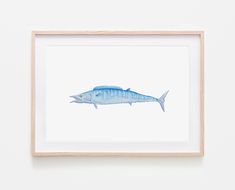 a watercolor painting of a blue fish on white paper in a wooden frame hanging on the wall