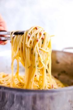 someone is holding a ladle full of spaghetti in their hand and lifting it from the pot