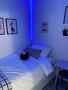 a bed with white sheets and blue lights in a room that has pictures on the wall