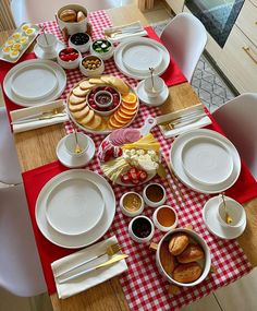 the table is set with plates, silverware, and other food on red checkered cloth