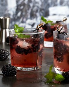 two glasses filled with blackberries and mint garnish on top of a table